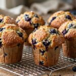 Tall bakery-style blueberry muffins with golden tops on a cooling rack